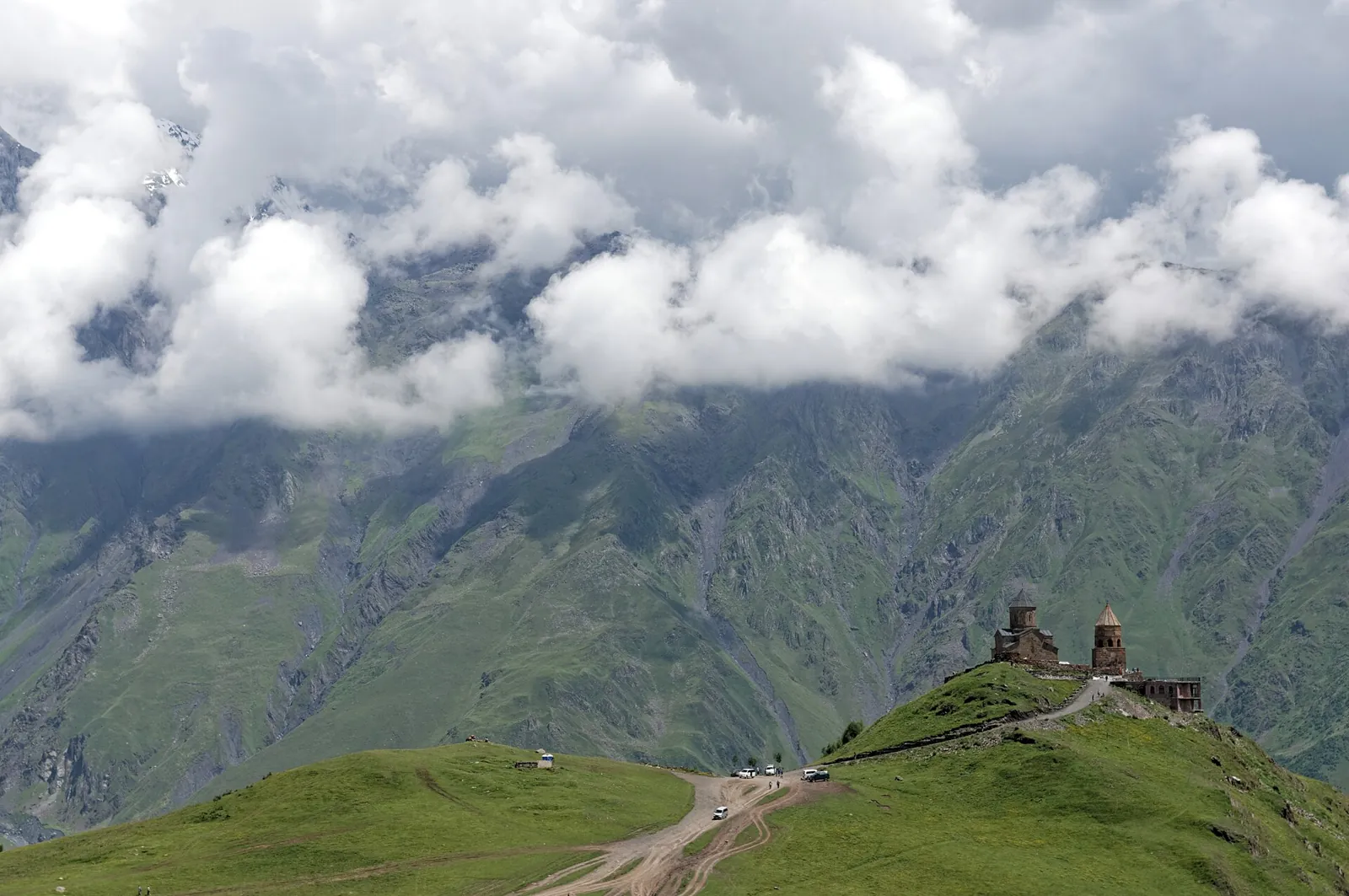 Gergeti Trinity Church on a green ridge below clouds and the Caucasus mountains near Kazbegi